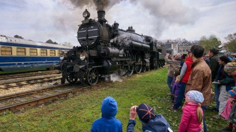 Eine Dampflock fährt und mehrere Personen stehen auf einer Wiese und schauen zu.