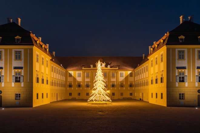 Blick auf das beleuchtete Schloss Hof vor dem ein beleuchteter Weihnachtsbaum steht.